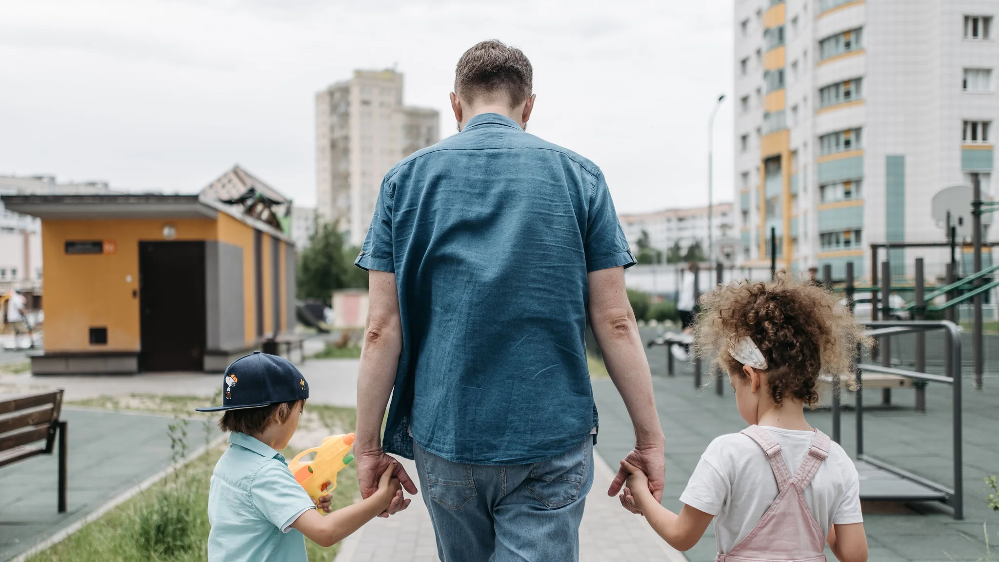 A father holding hands with two children at an outdoor playground